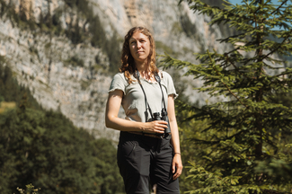 Daniela Schmocker steht in einer Wiese mit einem Feldstecher in der Hand