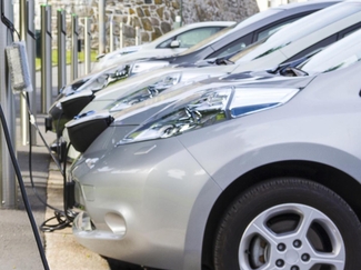 Seitliche Aufnahme mehrerer EVs die an zahlreichen Charging Stations aufgeladen werden. 