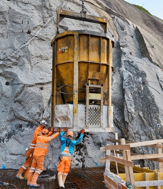 Ein Betonbehälter wird von Arbeitern an die richtige Stelle bugsiert